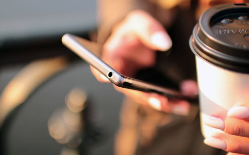 Person holding a smartphone and a takeaway coffee cup while texting outdoors.
