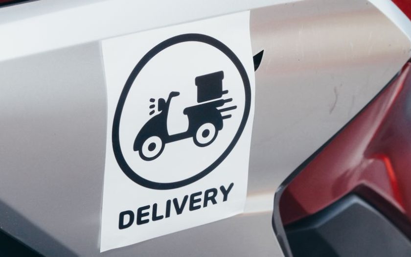 A delivery sticker featuring a scooter on a motorcycle's metallic surface.