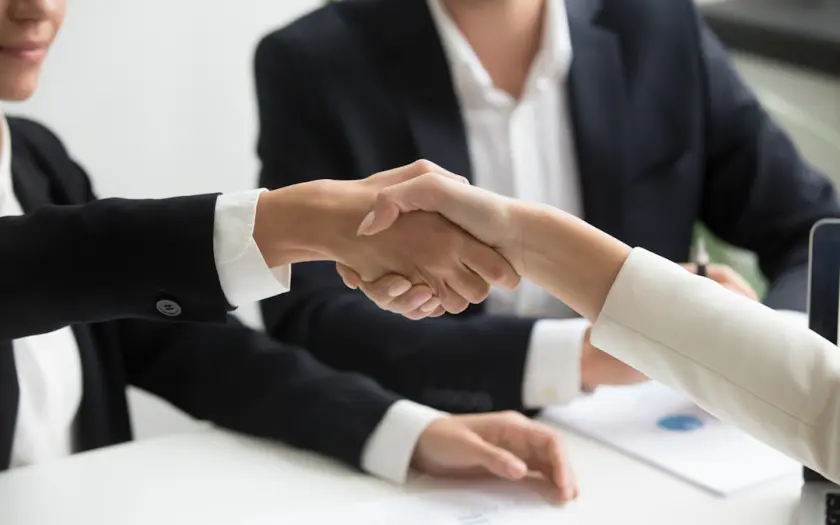 two people shaking hands in front of a laptop